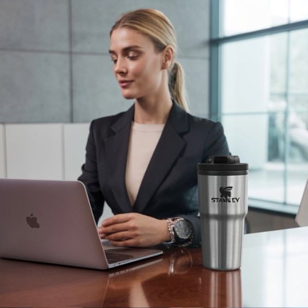 Femme au travail avec une stanley cup en inox posé sur son bureau
